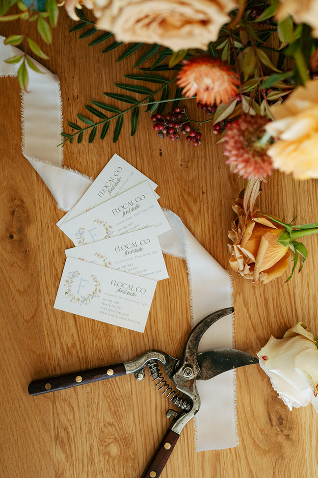 Floral arrangement with cut flowers, Flocal Co business cards and scissors on a wooden surface