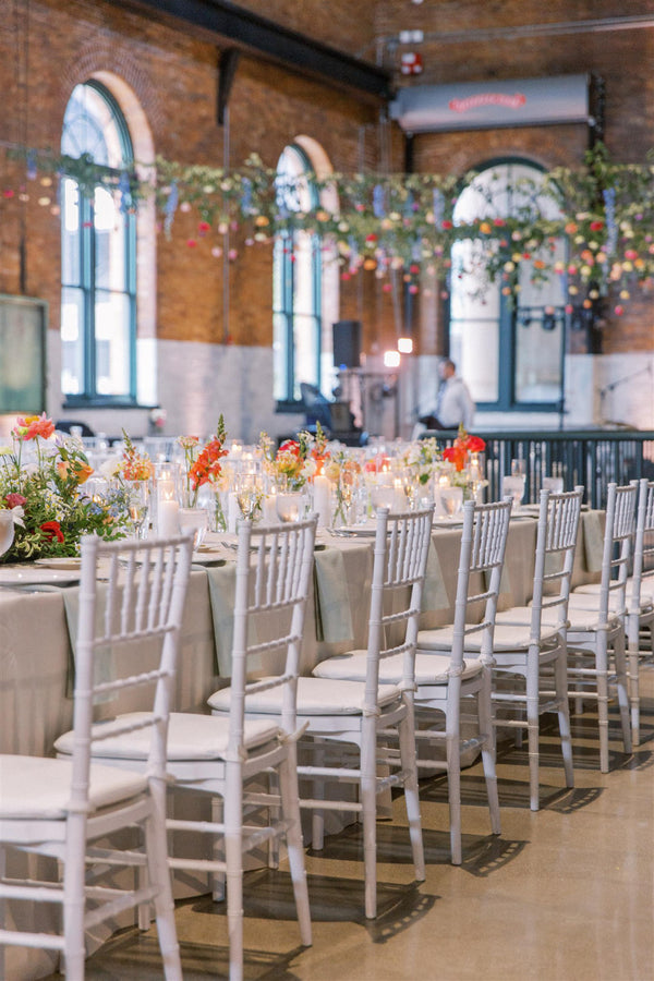 Indoor wedding reception featuring white chairs adorned with floral arrangements, creating a romantic atmosphere.