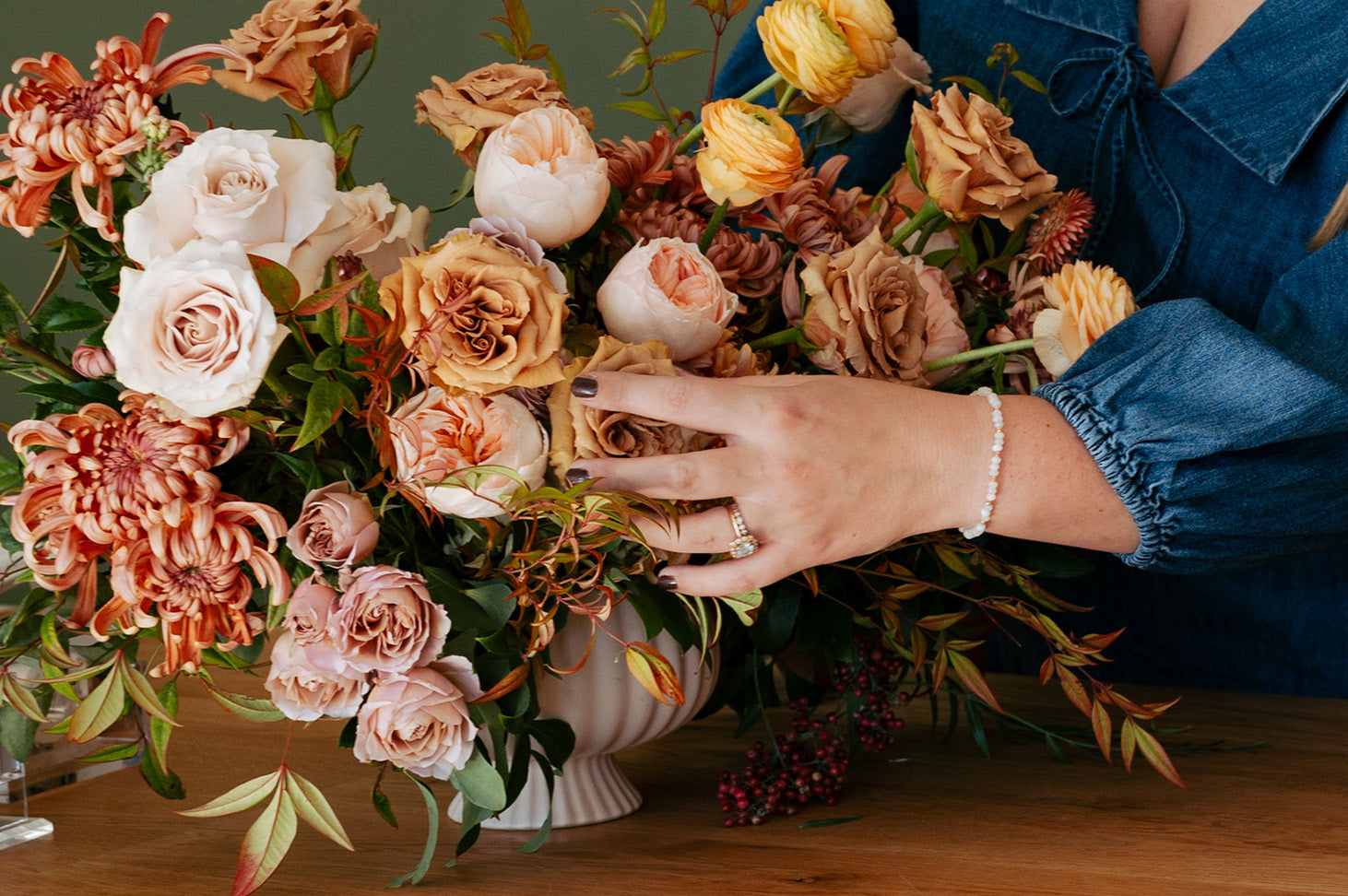 Grandview Heights florist touching a floral bouque that has pink, orange and blush flowers.