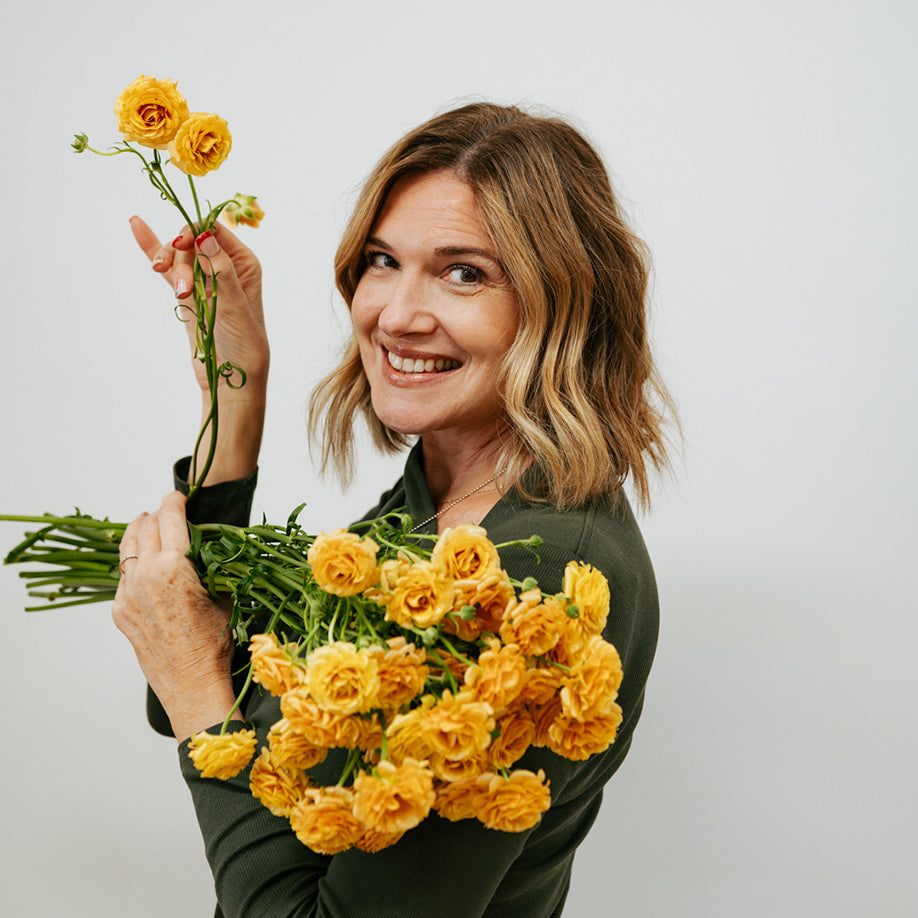 Woman holding a bouquet of yellow flowers against a plain background