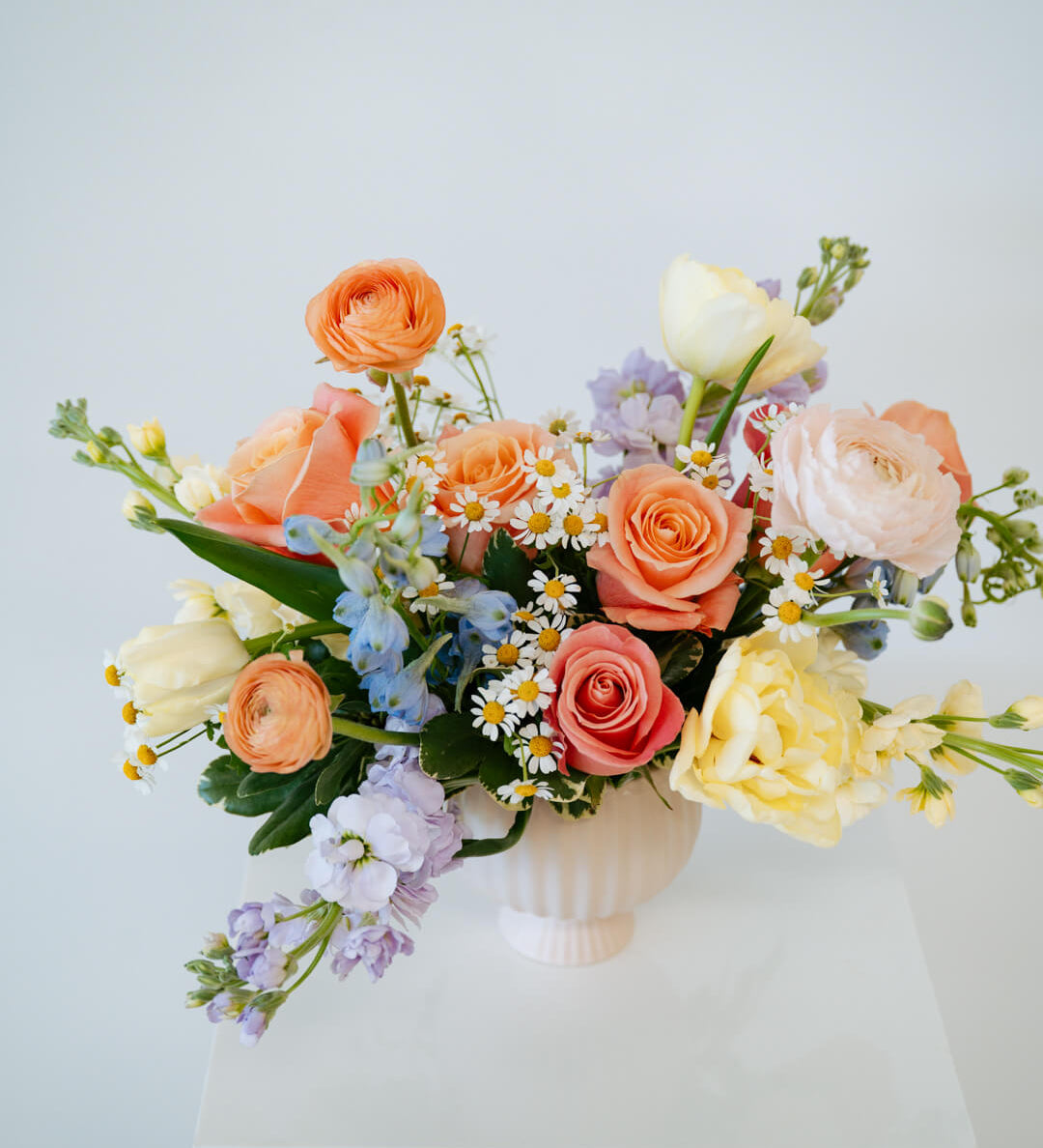 Medium April Showers arrangement showcasing spring blooms in a blush mini compote on a white pedestal. Available for local pick-up and delivery in the Columbus Ohio area 