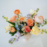 Medium April Showers arrangement showcasing spring blooms in a blush mini compote on a white pedestal. Available for local pick-up and delivery in the Columbus Ohio area 