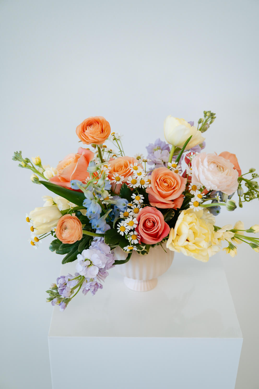 Medium April Showers arrangement showcasing spring blooms in a blush mini compote on a white pedestal. Available for local pick-up and delivery in the Columbus Ohio area 