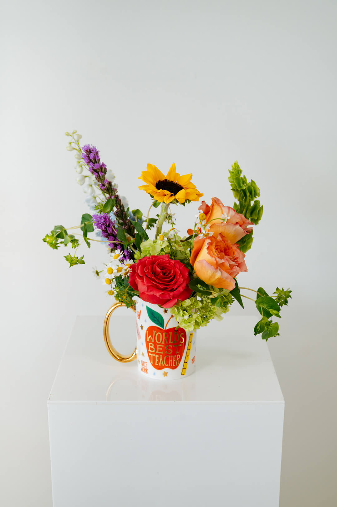 Colorful bouquet of flowers in a mug that reads Worlds Best Teacher available for local pickup and delivery in Columbus Ohio for teacher appreciation gifting