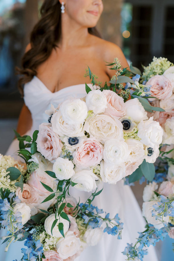 A radiant bride smiles while holding a bouquet of white and blue flowers, showcasing her elegance on her special day.
