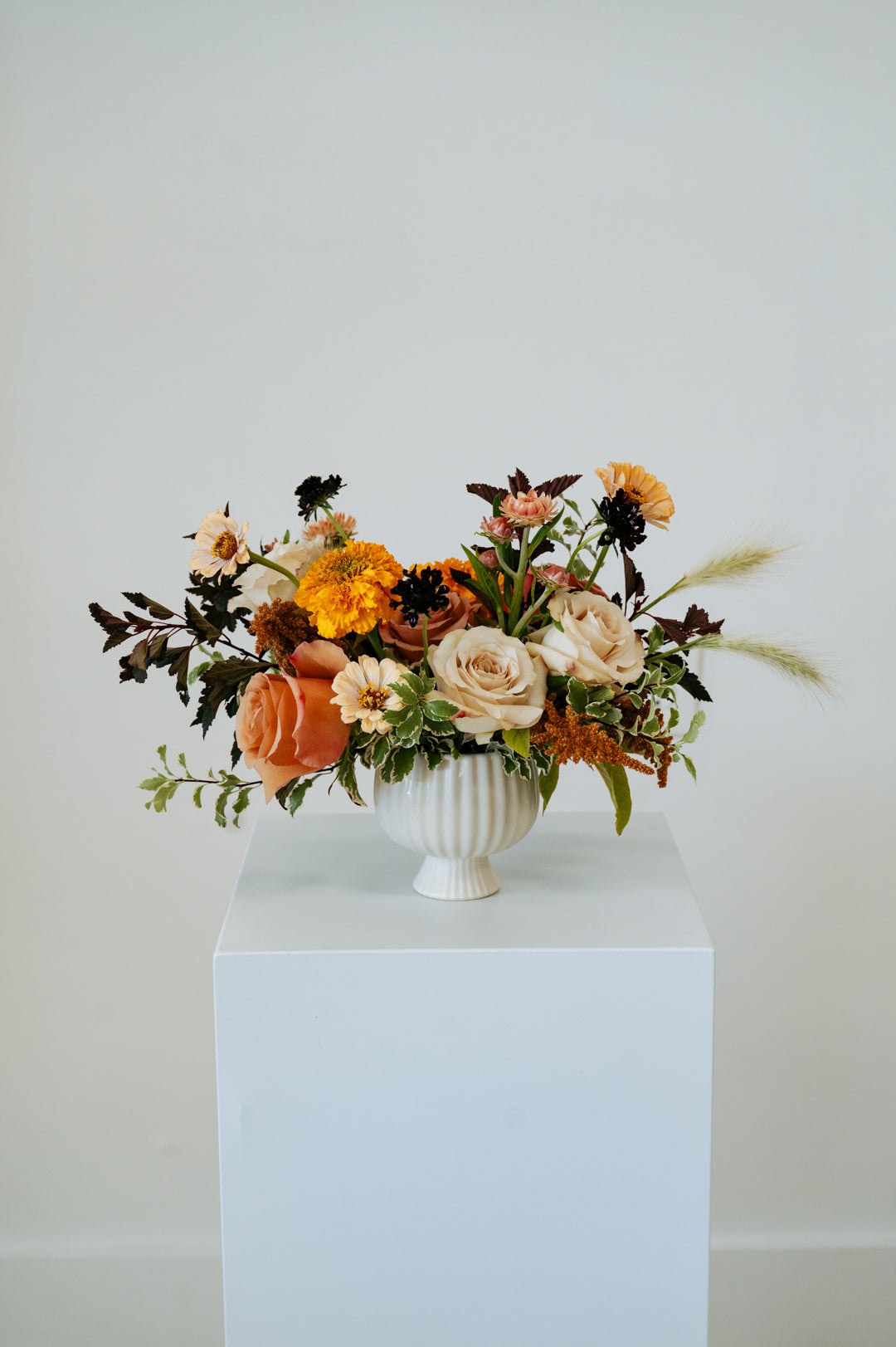 Floral arrangement in a white vase on a pedestal against a plain background available for local delivery and pick-up in Central, Ohio