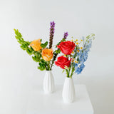Two small floral arrangements in white vases on a white surface with a light gray background