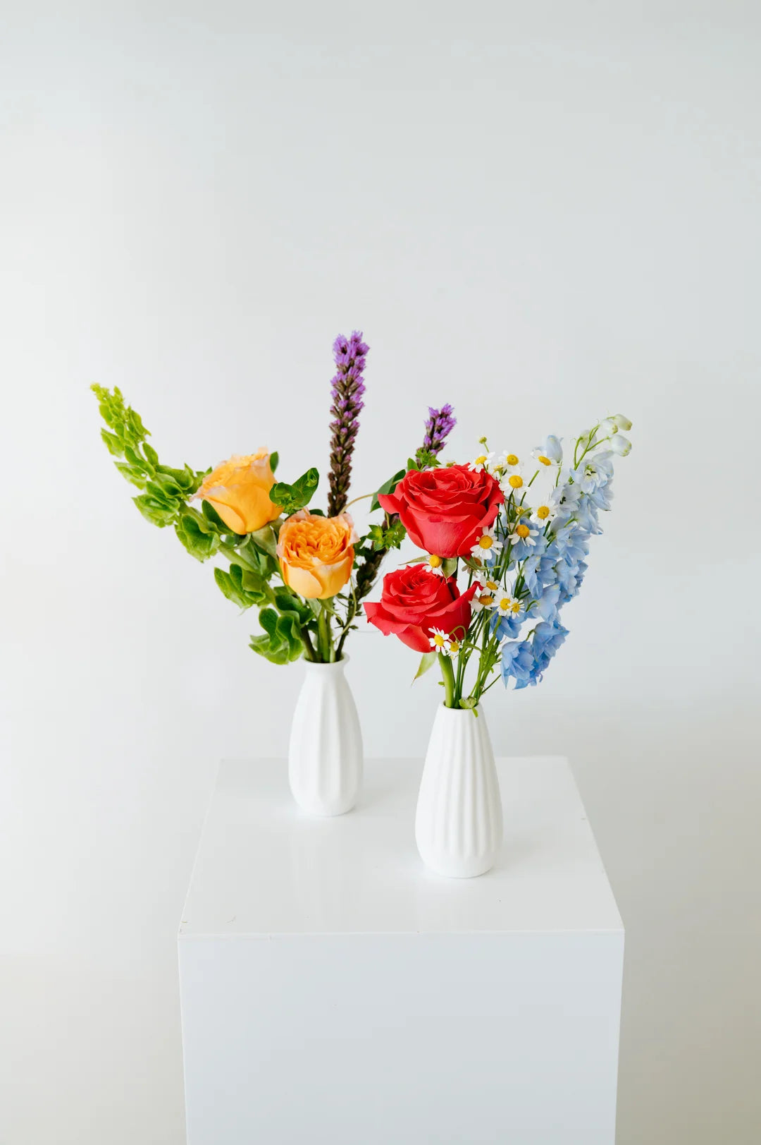 Two small floral arrangements in white vases on a white surface with a light gray background