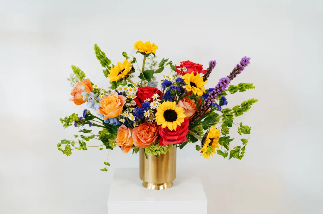 Colorful flower arrangement in a gold vase on a white background