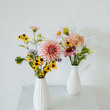 Two white ceramic vases filled with a mixed floral arrangement on a white pedestal against a white wall made by Flocal Co in Columbus Ohio