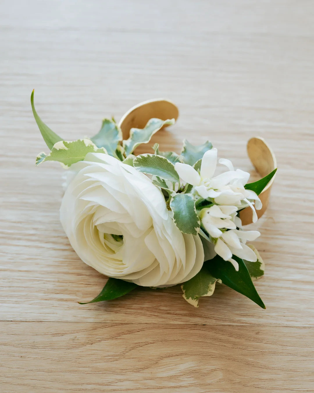 Floral wrist corsage with white flowers and green leaves on a light wooden surface