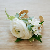 Floral wrist corsage with white flowers and green leaves on a light wooden surface