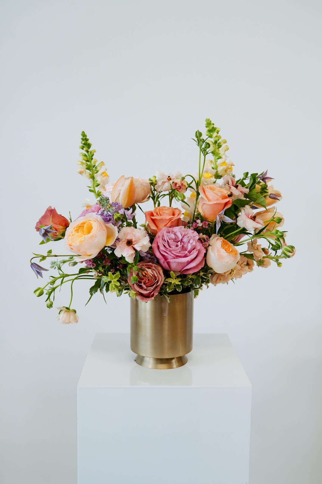 Large sized spring flower arrangement set in a gold vase on a white pedestal and neutral background. Available for same day local delivery and pickup in Columbus Ohio 