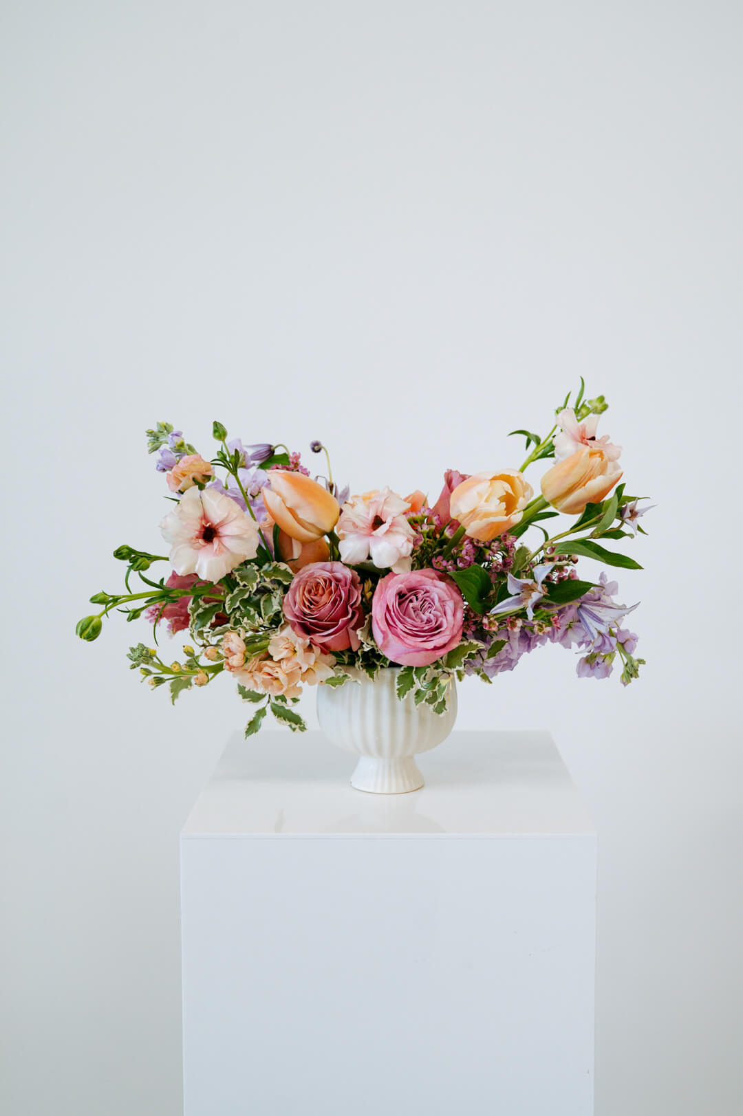 Medium sized spring flower arrangement set in a white vase on a white pedestal and neutral background. Available for same day local delivery and pickup in Columbus Ohio 