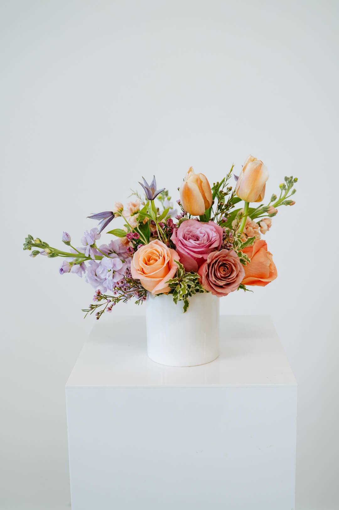 Petite sized spring flower arrangement set in a white vase on a white pedestal and neutral background. Available for same day local delivery and pickup in Columbus Ohio 