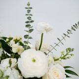 Close-up of a Columbus OH bouquet of white flowers with green leaves on a light gray background