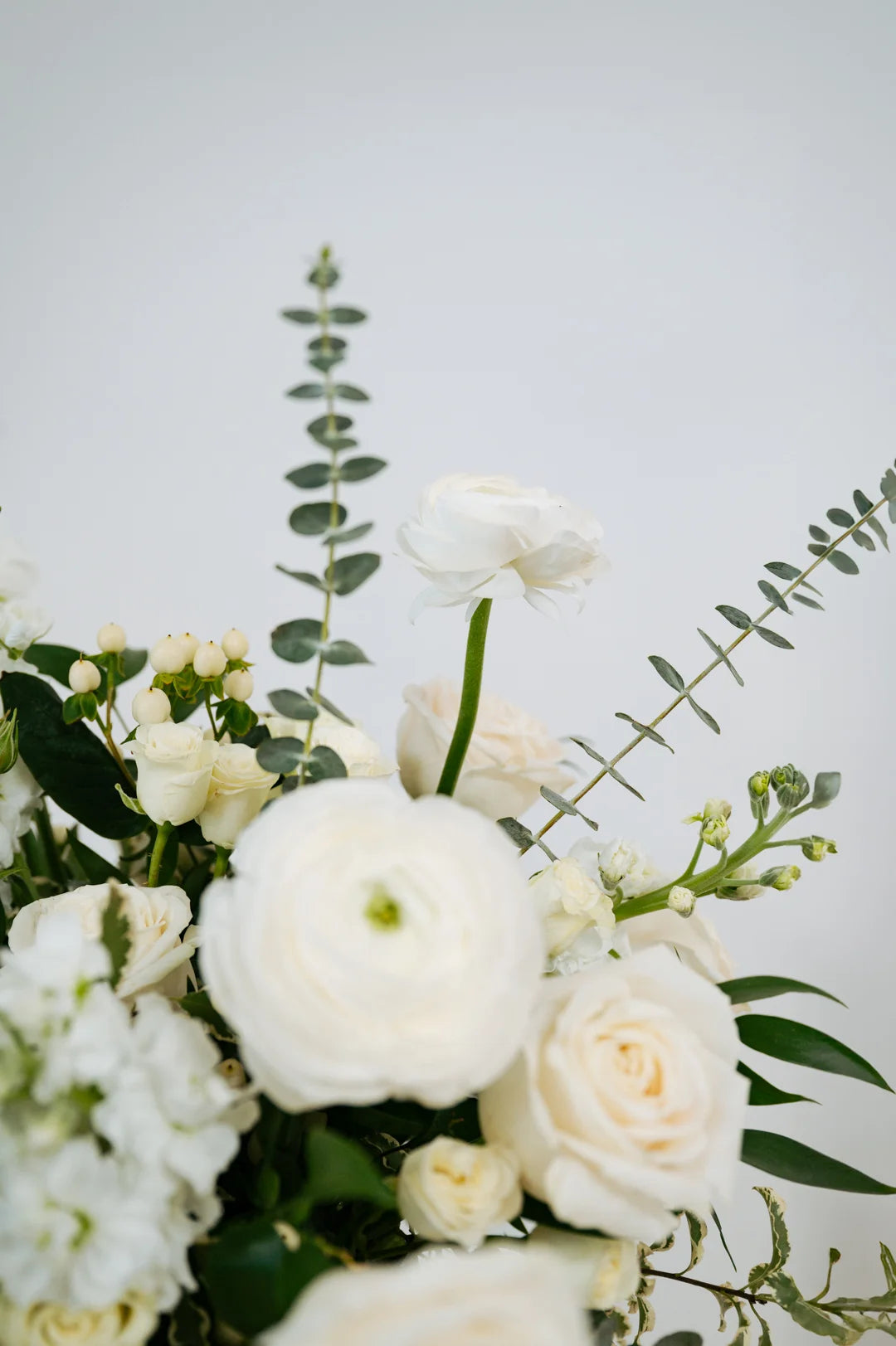 Close-up of a Columbus OH bouquet of white flowers with green leaves on a light gray background