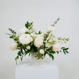 White and green Columbus floral arrangement in a white vase on a white surface with a light gray background