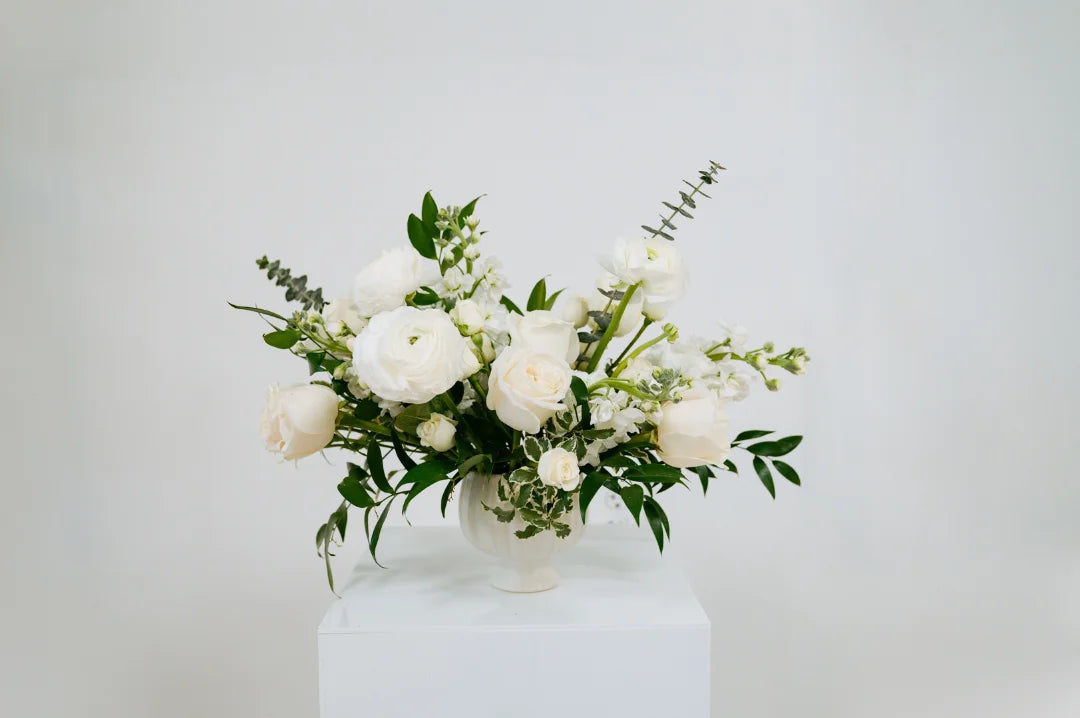 White and green Columbus floral arrangement in a white vase on a white surface with a light gray background