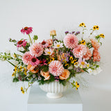 A vibrant wildflower bouquet in a white ribbed ceramic urn, displayed on a white pedestal against a clean white background made by Flocal Co in Columbus, Ohio