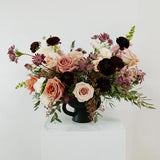 Large floral arrangement in a black vase on a white surface with a white background