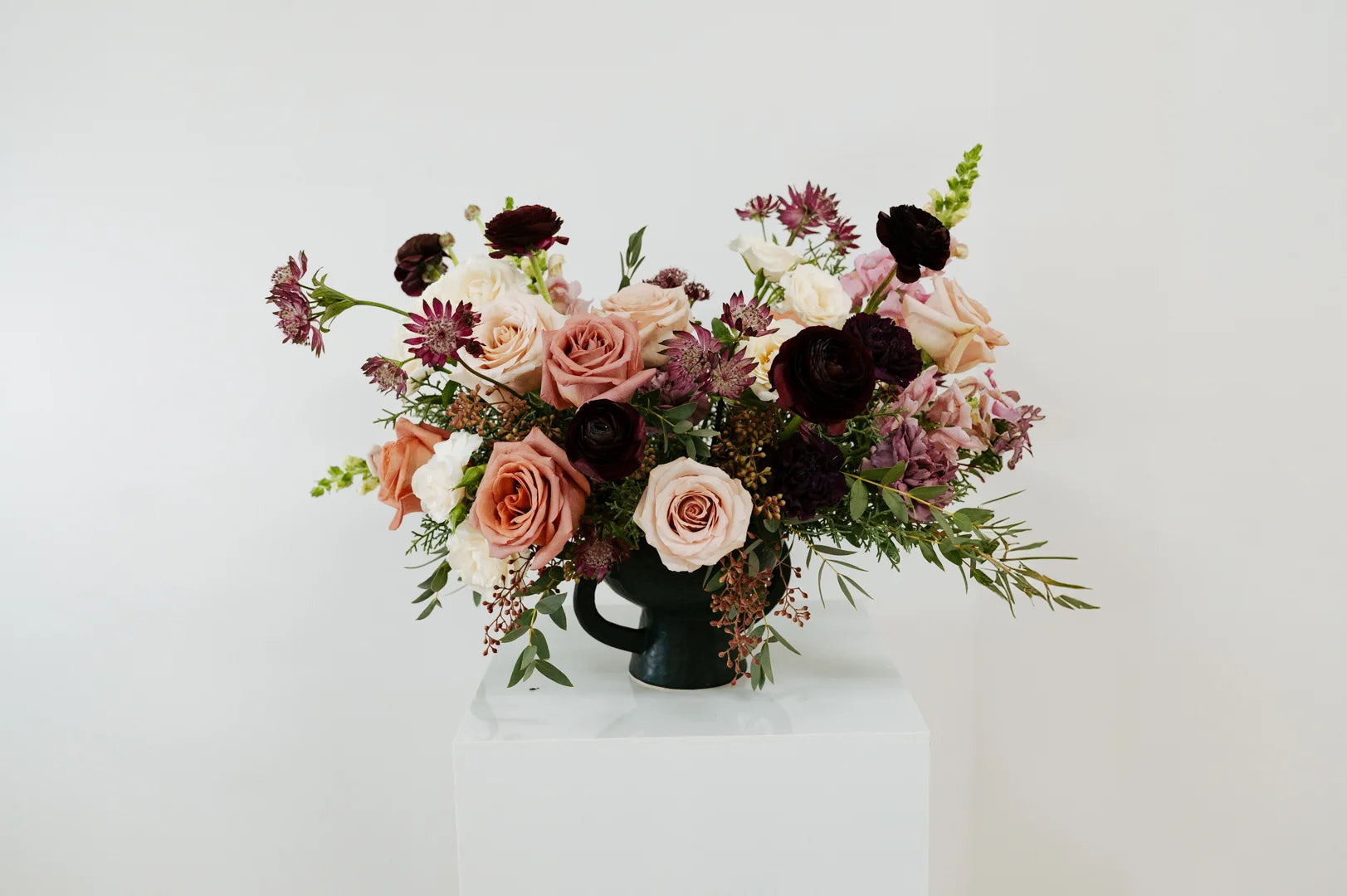 Large floral arrangement in a black vase on a white surface with a white background