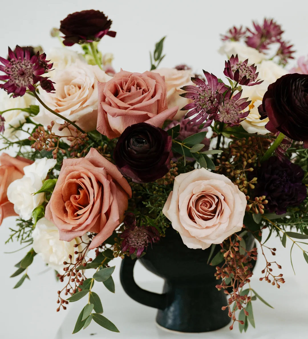 Large mauve flower arrangement with pink and white roses in a black vase on a white background