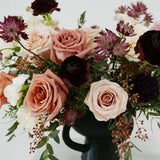 Large mauve flower arrangement with pink and white roses in a black vase on a white background