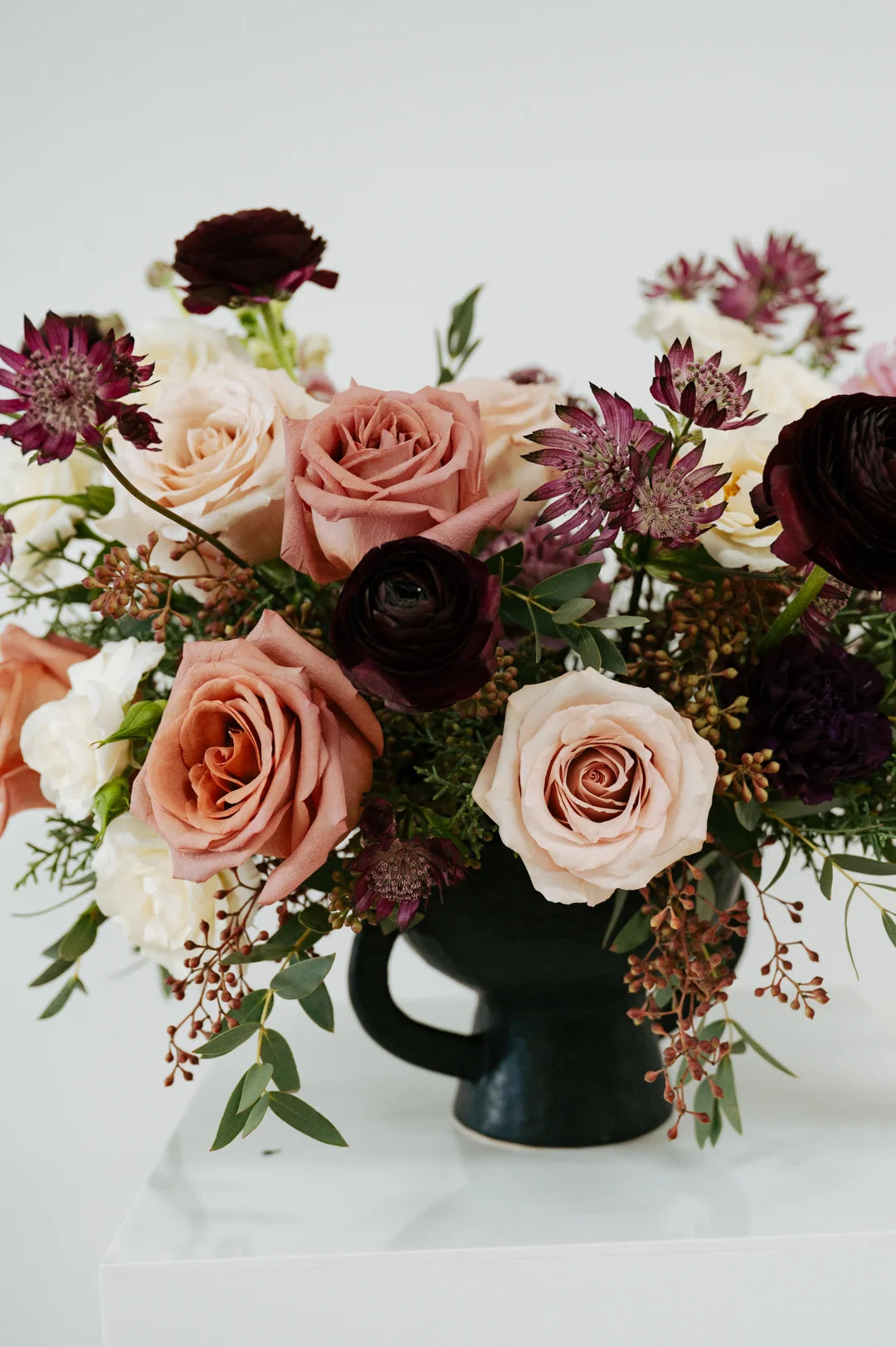Large mauve flower arrangement with pink and white roses in a black vase on a white background