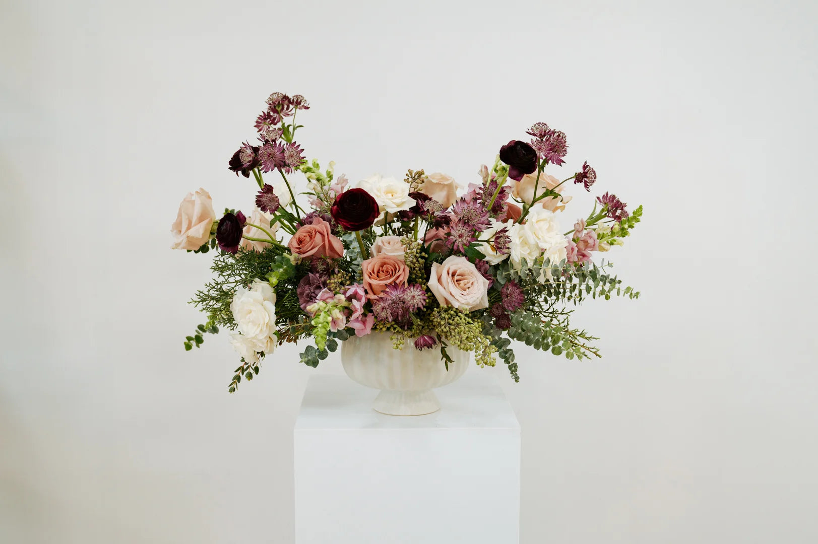 Moody mauve floral arrangement in a white vase on a white surface with a light gray background