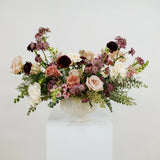 Moody mauve floral arrangement in a white vase on a white surface with a light gray background