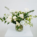 Bouquet of white flowers in a clear vase on a white surface with a light gray background at Flocal Co.