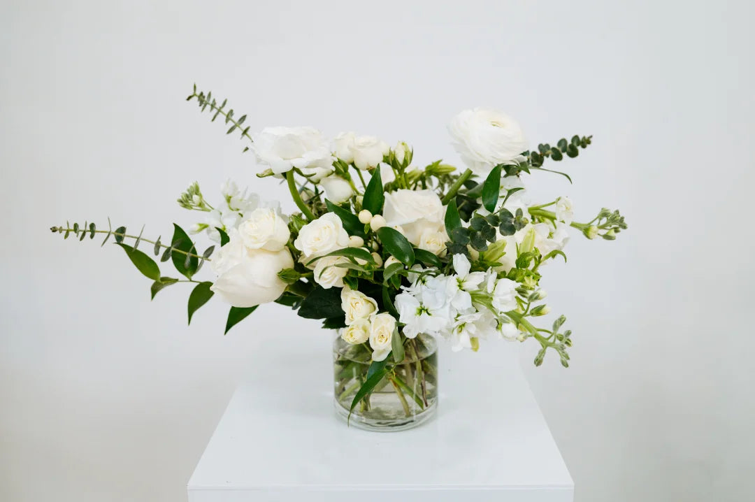 Bouquet of white flowers in a clear vase on a white surface with a light gray background at Flocal Co.