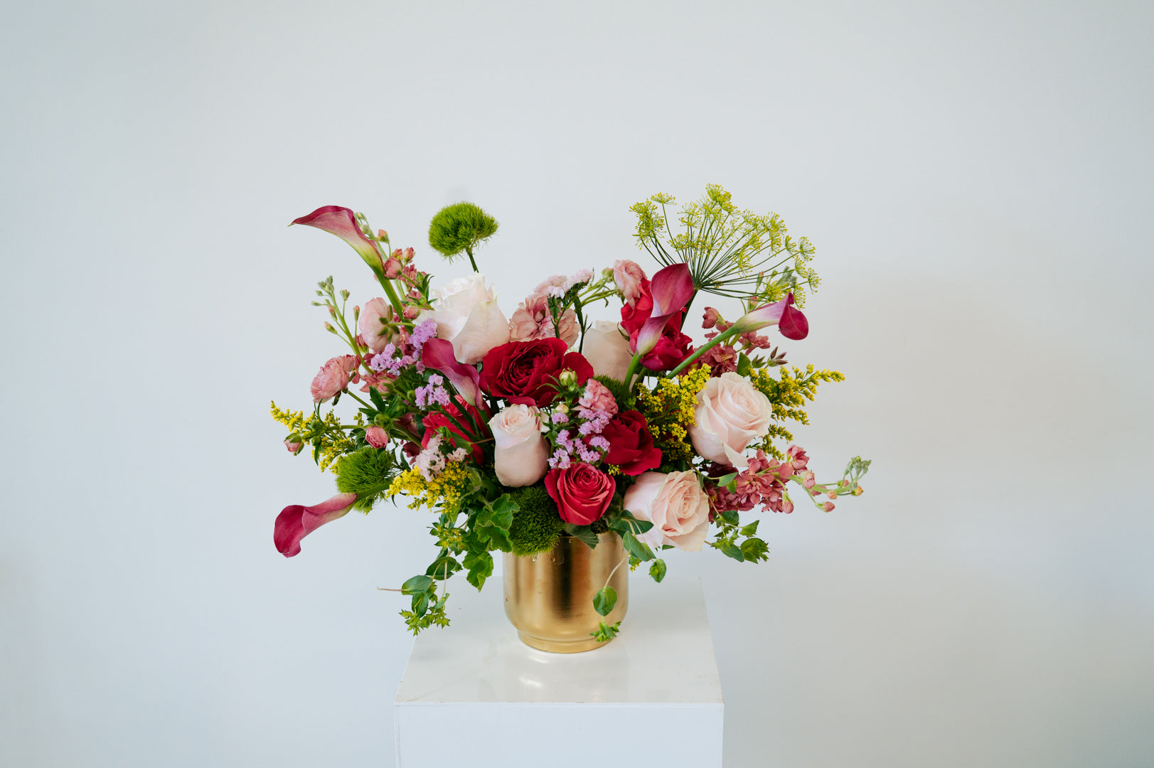 Large statement sized spring flower arrangement set in a gold vase on a white pedestal and neutral background. Available for same day local delivery and pickup in Columbus Ohio 