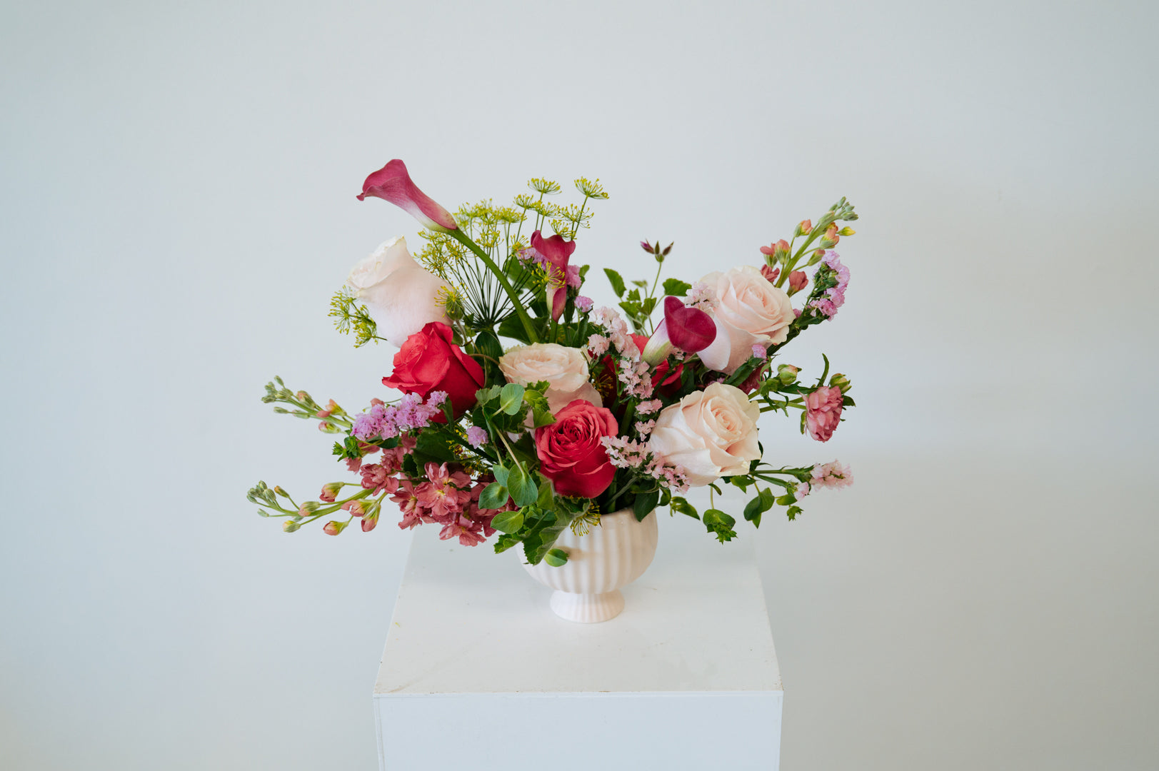 Medium compote sized spring flower arrangement set in a neutral mini compote on a white pedestal and neutral background. Available for same day local delivery and pickup in Columbus Ohio 