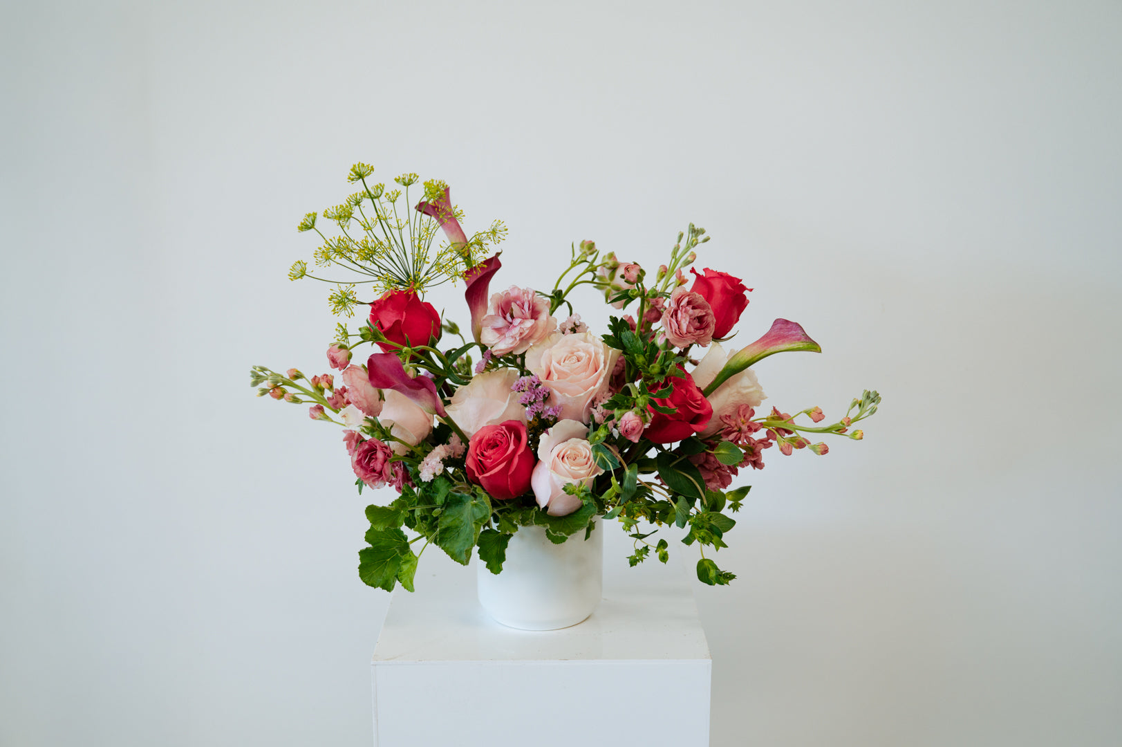 Petite sized spring flower arrangement set in a white vase on a white pedestal and neutral background. Available for same day local delivery and pickup in Columbus Ohio 
