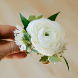 White flower corsage held by a hand against a beige background