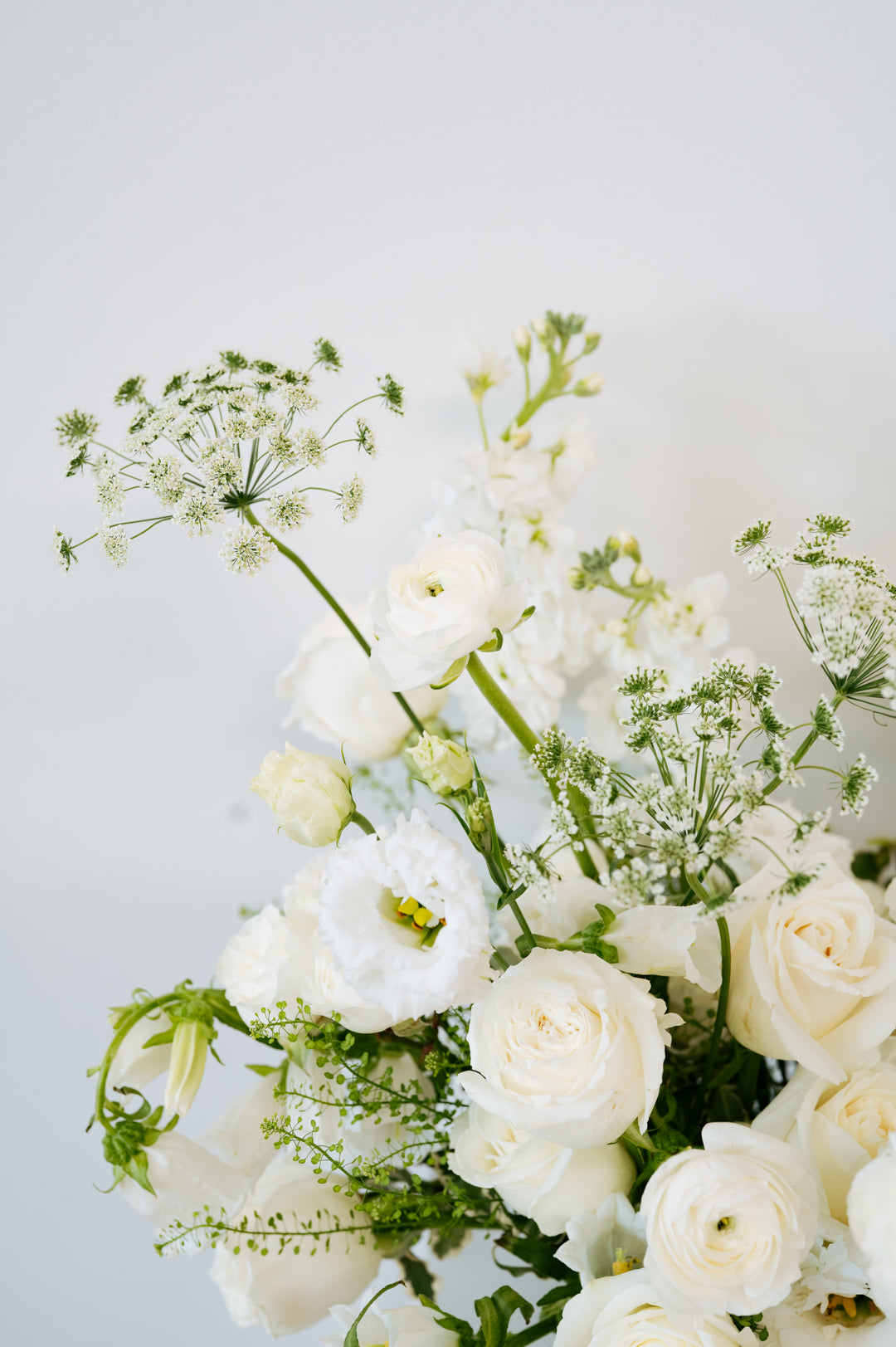 A close-up of a white floral bouquet featuring roses, ranunculus, and delicate green foliage against a soft light gray background available for pick-up and delivery in Columbus, Ohio