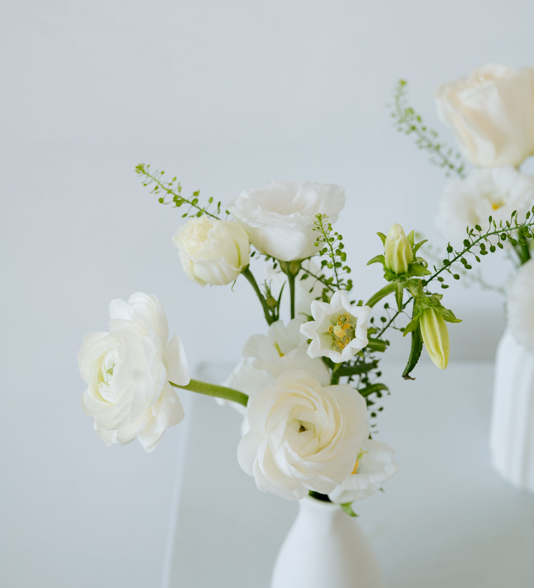 A small white ceramic vase holding a bouquet of white flowers, including roses and lilies, with green stems, set against a clean white background available for local delivery and pick up in Columbus Ohio