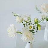 A small white ceramic vase holding a bouquet of white flowers, including roses and lilies, with green stems, set against a clean white background available for local delivery and pick up in Columbus Ohio