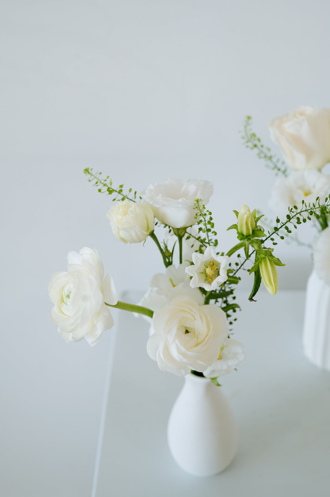A small white ceramic vase holding a bouquet of white flowers, including roses and lilies, with green stems, set against a clean white background available for local delivery and pick up in Columbus Ohio