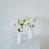 Two white ceramic vases with white flowers and green stems, displayed on a white pedestal against a light gray wall available for pick-up and local delivery in Columbus, Ohio